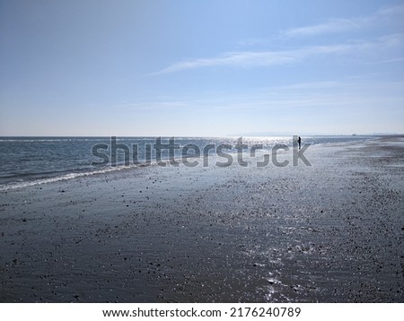 Long distance view of an empty calm beach with a single person silhouette in distant view. The sun is setting but the sky is still blue on this spring evening. The sea is calm and gentle.