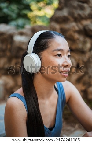 Asian sport girl listening to music on white wireless headphones while resting from running.
