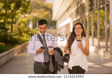 Latino man and woman walk through the financial center of Guatemala. Young business couple. Office workers walk in the city holding a cup of coffee. Royalty-Free Stock Photo #2176255493