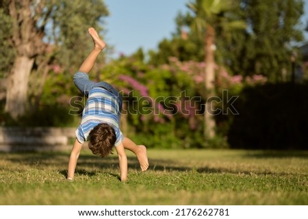 Mischievous preschooler boy somersaults on sand grass in the park. Royalty-Free Stock Photo #2176262781