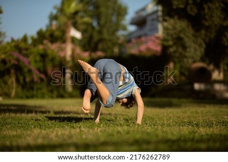Mischievous preschooler boy somersaults on sand grass in the park. Royalty-Free Stock Photo #2176262789