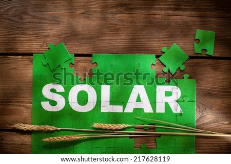 Pieces of jigsaw puzzle on a wooden board with a word SOLAR written on them.