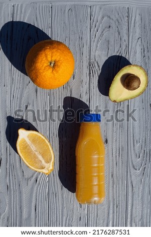 An appetizing composition of a bottle of orange juice, half a lemon, orange and a ripe avocado, on a light, textured, wooden background, in the kitchen.