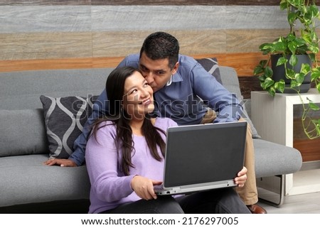 Latino adult man and woman couple use their laptop in the living room to shop online, make payments, plan trips, view photos and make video calls
