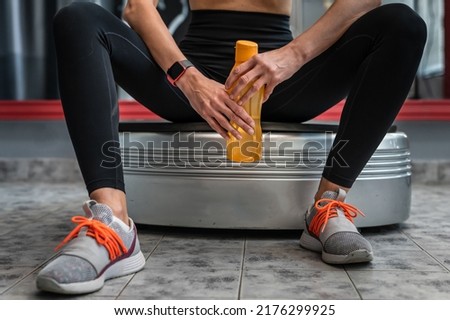 Midsection of unknown caucasian woman female athlete holding plastic bottle of water while taking a brake resting during training sitting on the power plate vibration platform copy space Royalty-Free Stock Photo #2176299925