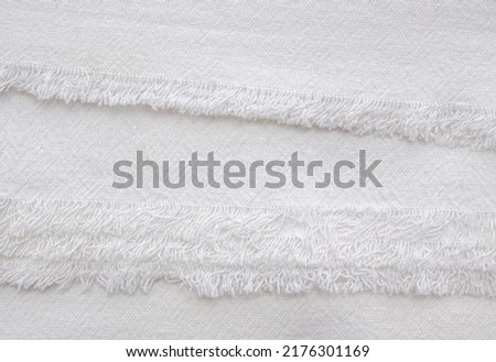 Abstract solid colored background with textile texture. A sample of plain white cotton fabric. The image of the edges of the fabric with fringe.   Royalty-Free Stock Photo #2176301169