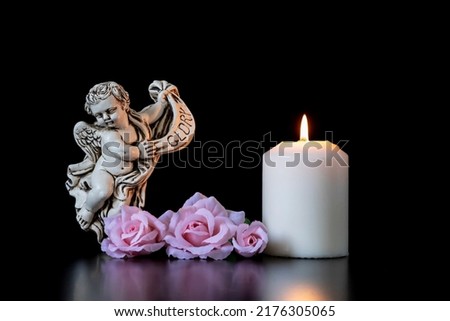CONDOLENCE CARD FOR ALL SAINTS DAY WITH AN ANGEL OF GLORY, CANDLE AND PINK ROSES ON BLACK BACKGROUND. COPY SPACE.