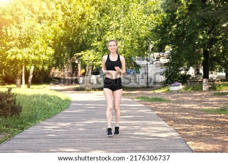 Full length photo of happy fit fitness athletic girl runner running, jogging, young beautiful woman is smiling training outdoors at summer sunny day in the morning in black top and shirts 