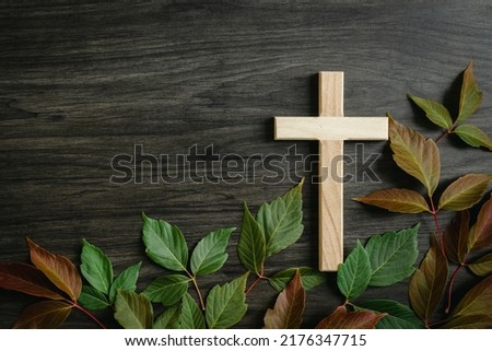 Wood cross with red and green autumn leaves on a dark wood background with copy space