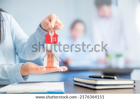 Real estate agent holding house key on table with house designs document,calculator,model house.Concept for real estate
