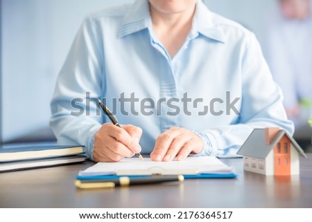 Close up of hand of the real estate agent drafting an agreement on the home insurance contract documents, along with samples of house models to present to his clients.