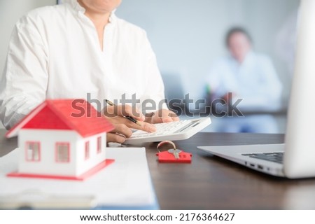 Small house model on wooden table and professional financial advisor is using calculator.