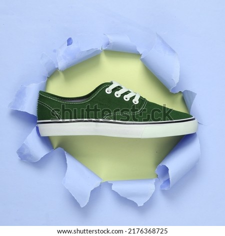 Sneaker through a torn hole on pastel background. Concept art. Pastel color trend. Minimalism