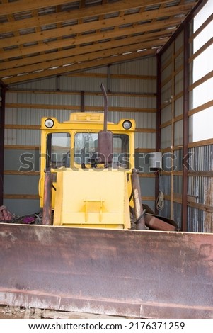 Large powerful yellow tractor with large wheels in the hangar, warehouse, garage with open gates