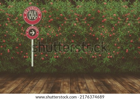 Restroom sign with red flower and green leaves wall background with wood floor.