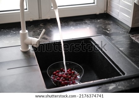 young woman washing cherries at home under running water to make juice