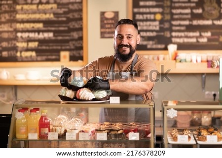 male coffee shop owner near showcase with cakes and desserts in his cafe, work in the bar cafeteria Royalty-Free Stock Photo #2176378209
