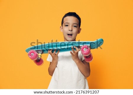 a little boy of preschool age stands on an orange background in a white T-shirt, smiling fervently holding his skate in front of him with his mouth open in surprise