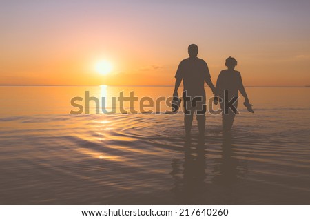 Senior couple walking holding hands in the water at sunset Royalty-Free Stock Photo #217640260