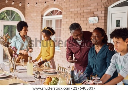 Happy mature African American man and his wife having fun while setting dining table for family lunch on patio.