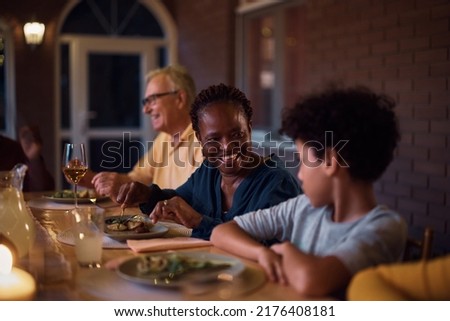 Happy African American grandmother and grandson communicating while eating dinner during family gathering at dining table. 