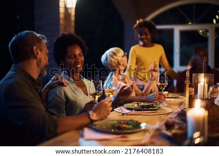 Happy multiracial couple talking and drinking wine while having dinner with their family at dining table on a patio.  