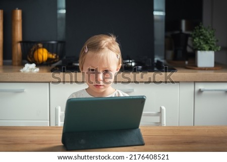 Cute little caucasian girl watching cartoons on tablet in the stylish interior
