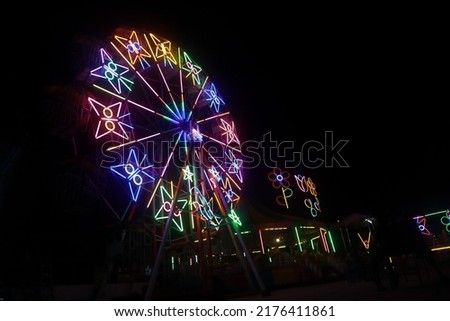 The colorful stars on the Ferris wheel glow at night at the fair. blurry black background