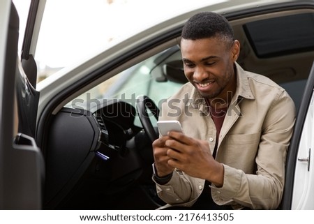 Happy smiling man typing a message on the phone while sitting in the car. Royalty-Free Stock Photo #2176413505