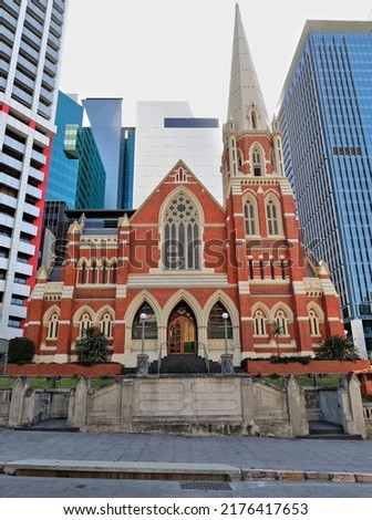 Victorian Gothic Revival architecture: Albert Street Uniting Church of red brick-white trimming-steeply pitched roof-tall spire-cruciform plan among modern skyscrapers. Brisbane-Queensland-Australia. Royalty-Free Stock Photo #2176417653