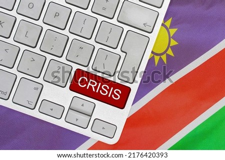 White computer keyboard with red button with word of crisis on Namibia flag background. Global economic, political and financial crisis. Economic crisis and economic recession in Namibia