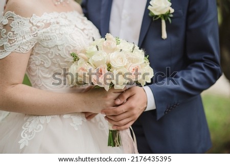 Wedding bouquet of roses in the hands of the bride and groom. Bridal bouquet of roses in the hands of the woman. Bouquet of lavander and roses: cream, white and pink. Groom boutonniere with white rose Royalty-Free Stock Photo #2176435395