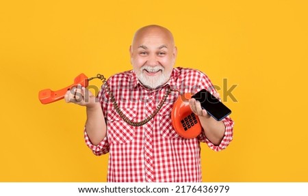 cheerful senior man with retro telephone and modern smartphone on yellow background