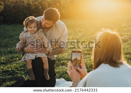 Young Family Having Picnic Outdoors, Woman Taking Pictures of Her Husband and Baby Daughter at Sunset