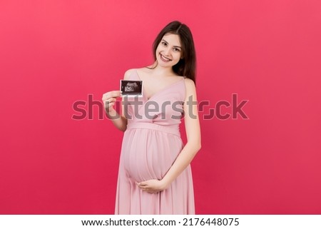 Cute Pregnant Lady Posing With Baby Sonography Photo Near Colored background. Concept of pregnancy, gynecology, medical test, maternal health.
