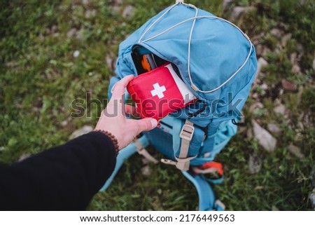A first aid kit is in a backpack, a hand holds a bag of medicines, an open pocket of a bag, road medicine assistance, camping equipment. High quality photo Royalty-Free Stock Photo #2176449563