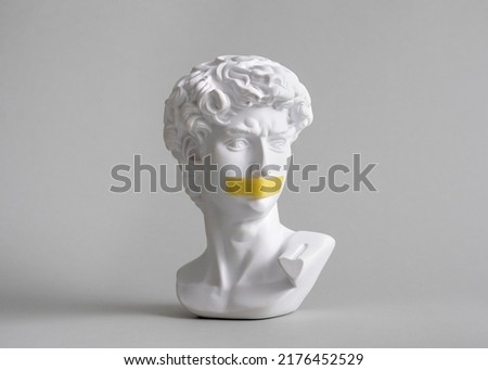 Michelangelo's David head bust in duct tape sealed mouth. Minimal concept on gray background censorship of freedom of speech and restrictions of thought and word. Fight for your rights. Royalty-Free Stock Photo #2176452529