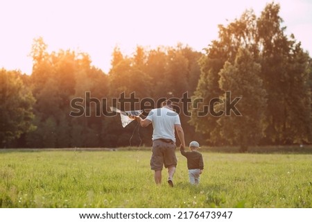 Family vacation. Summer outdoor photo of a father and son flying a kite in a meadow. A picture against the sun. Warm family moments or a conceptual image for spending time outdoors.