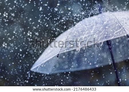 Transparent umbrella under heavy rain against water drops splash background. Rainy weather concept. Royalty-Free Stock Photo #2176486433