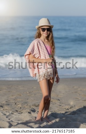 Portrait of a girl in a hat and black glasses in full growth on the background of the sea. Vertical shot.