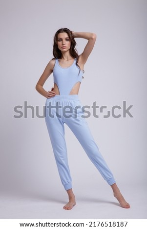 High fashion photo of a beautiful elegant young  woman in a pretty blue body slim, pants posing on white background. Slim figure, studio shot. Brunette, long hair