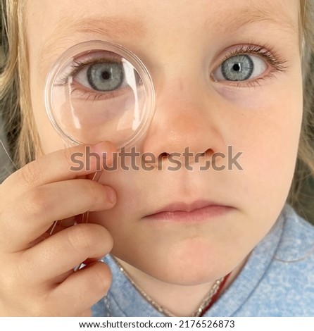 
a little girl with blue eyes looks through a magnifying glass. child playing