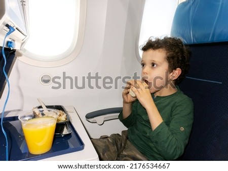 cute little boy in airplane seat eating while looking at the screen
