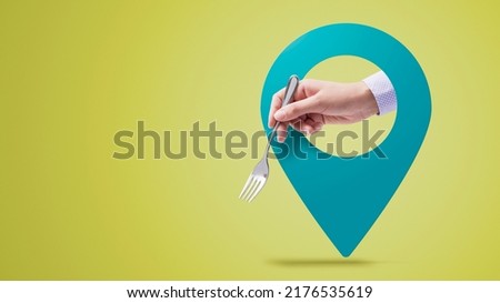 Hand holding a fork and location pin: find restaurants near you concept Royalty-Free Stock Photo #2176535619