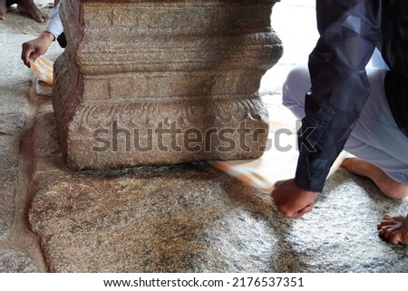The incredible amazing hanging pillar, Veerabhadra Shiva temple, Lepakshi, Andhra. Visitors passing a towel underneath the pillar to test if there is a gap between the floor and the pillar.            Royalty-Free Stock Photo #2176537351