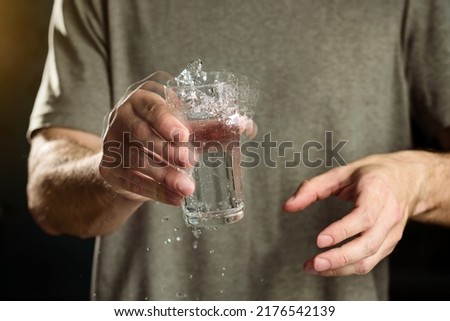 A man holds a glass of water with a shaking hand. The concept of parkinson's disease and tremor. Royalty-Free Stock Photo #2176542139