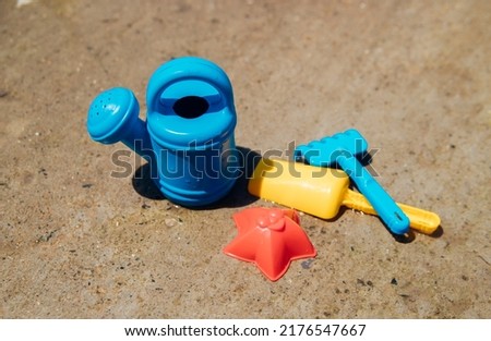 A set of children's toys for playing in the sandbox. Colored rake, shovel, watering can made of plastic, close-up. Early development of the child, the concept of children's leisure.