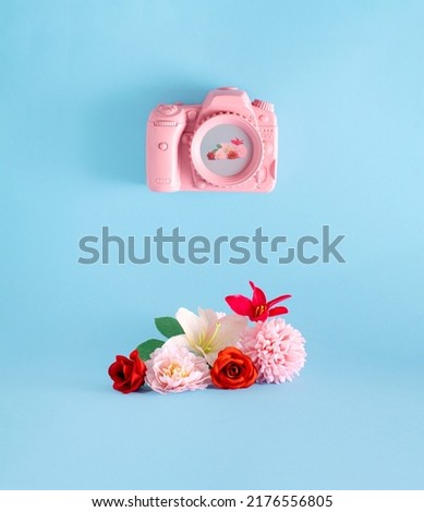 Pastel pink photo camera and floral arrangement, creative layout, pastel blue background.