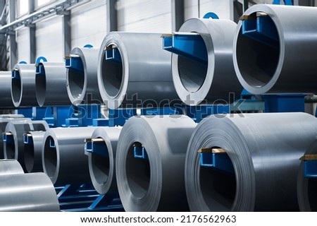 Large rolls of electrical transformer steel strips hang on blue metal rack in spacious warehouse of production plant close view Royalty-Free Stock Photo #2176562963