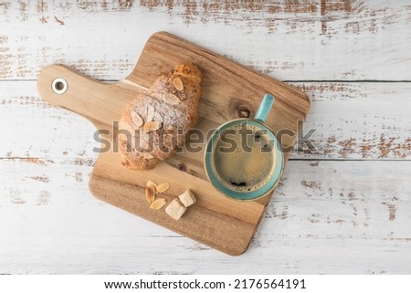 Fresh baked almond nuts breakfast croissant and hot coffee cup on rustic wooden background. Top view pastry good morning card with copy space